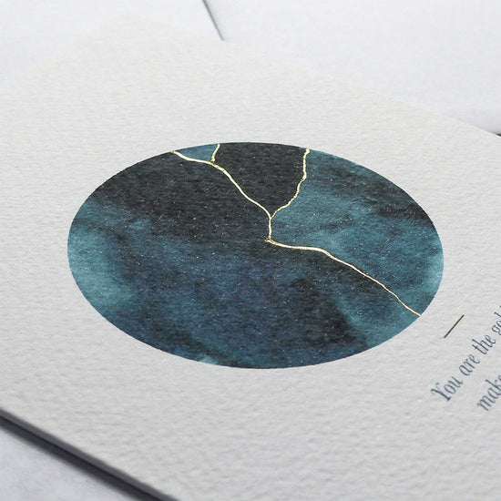 This A6 watercolour Kintsugi greeting card is printed at our studio & features an inky blue watercolour circle with hand-finished gold lines added.