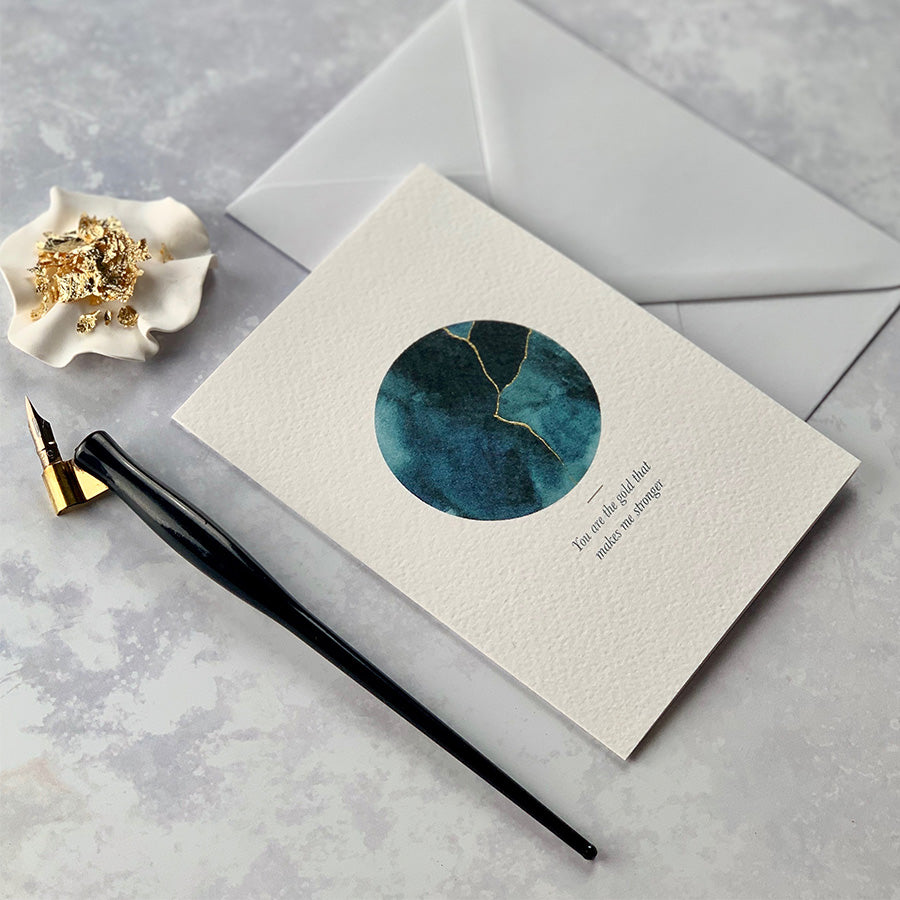 
                      
                        This A6 watercolour Kintsugi greeting card is printed at our studio & features an inky blue watercolour circle with hand-finished gold lines added.
                      
                    