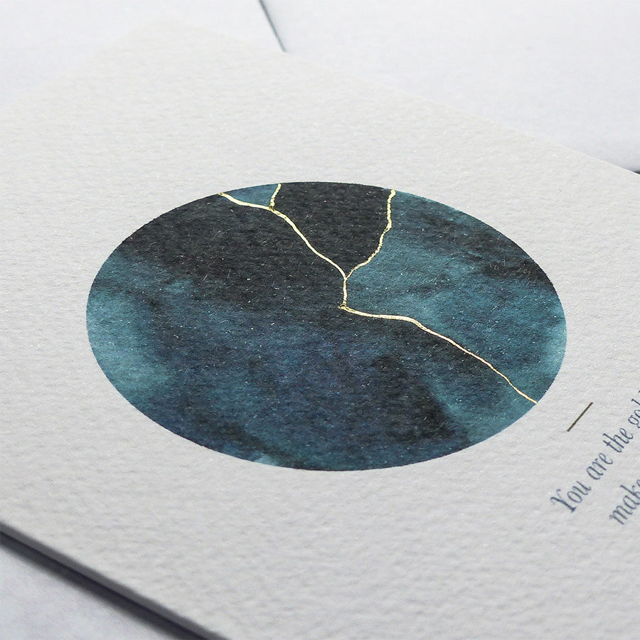 
                      
                        This A6 watercolour Kintsugi greeting card is printed at our studio & features an inky blue watercolour circle with hand-finished gold lines added.
                      
                    